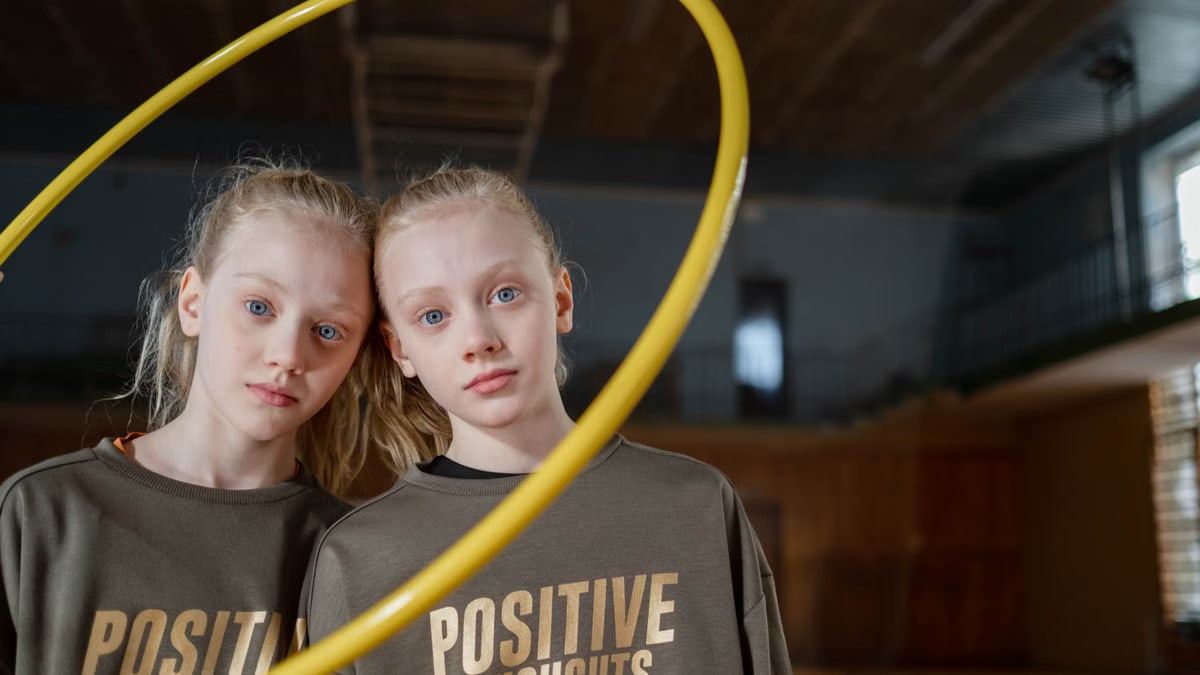 Twin girls in sportswear indoors with a hula hoop expressing positivity. Perfect for family and sports themes.