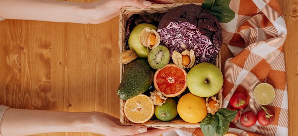 Vibrant basket of fresh fruits and vegetables with hands holding on a wooden table.