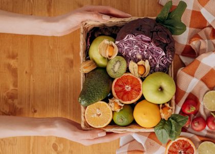 Vibrant basket of fresh fruits and vegetables with hands holding on a wooden table.