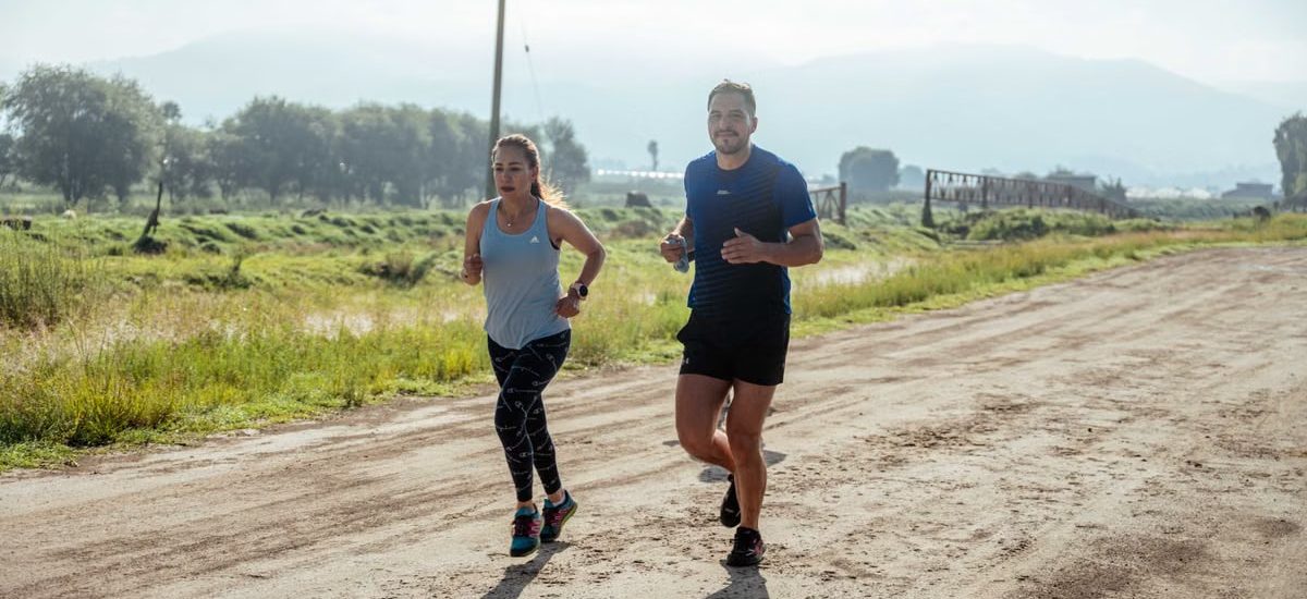 Active couple jogging on a dirt road in a scenic rural area under the bright sun.