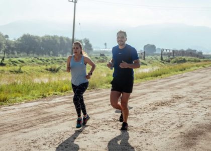 Active couple jogging on a dirt road in a scenic rural area under the bright sun.